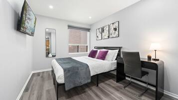 A modern bedroom with a bed, desk, chair, and artwork on the wall.