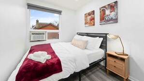 A bedroom with a bed, a nightstand, a lamp, and two paintings on the wall. - Modern Suite Near Dufferin Grove Transit Line (Toronto)