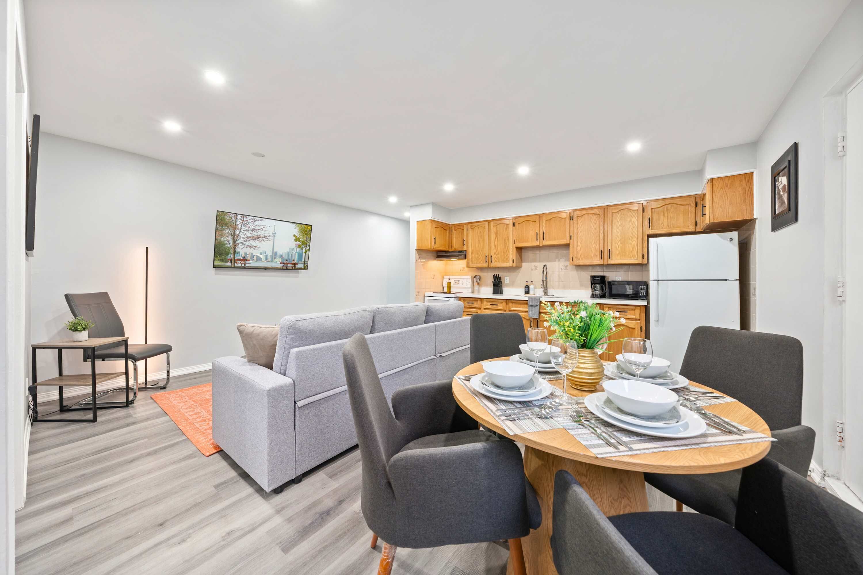 A modern living space with a dining area, grey sofa, wooden dining table, and kitchen in the background.