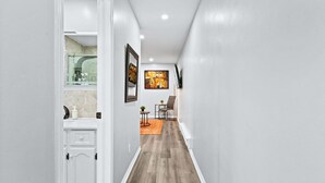 A hallway with a wooden floor, white walls, a small table with chairs, and a painting on the wall. - Modern Suite Near Dufferin Grove Transit Line (Toronto)