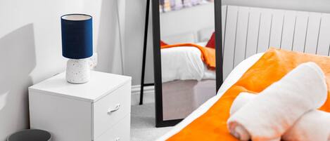 Un dormitorio con una cama, una mesita de noche con lámpara, un espejo y un radiador.