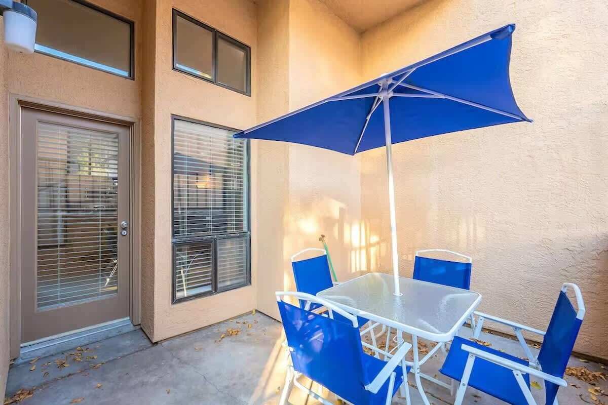 Une terrasse extérieure avec une table et des chaises, un parasol bleu et une porte avec des stores.