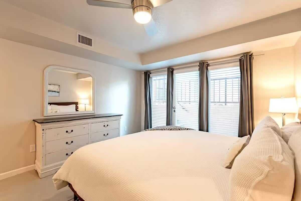 Un dormitorio con cama, cómoda, espejo y ventana con cortinas.