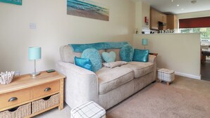 Een woonkamer met een beige bank, kussens in teal, een houten bijzettafeltje en een schilderij aan de muur.