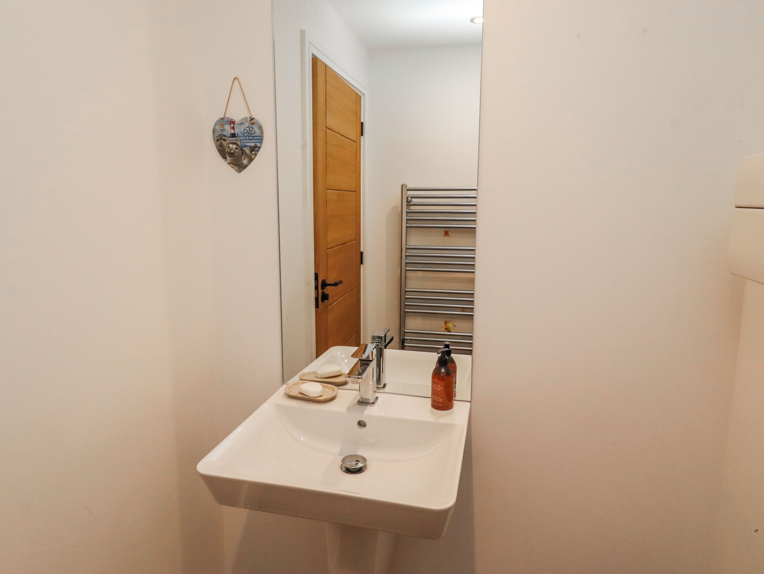 A bathroom with a white sink, a mirror, a towel, and a soap dispenser.