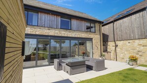 A modern two-story house with a stone facade, large glass windows, and a patio with outdoor furniture. - The Joiners Cottage (Morpeth)