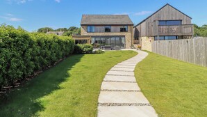 A modern two-story house with a stone facade, a wooden deck, and a well-maintained lawn. - The Joiners Cottage (Morpeth)