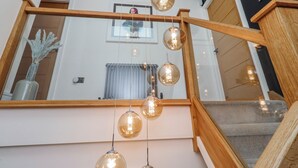 A staircase with a wooden handrail and glass pendant lights. - The Joiners Cottage (Morpeth)
