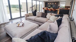 A modern living room with a sectional sofa, a coffee table with chess pieces, and a tripod in the background. - The Joiners Cottage (Morpeth)