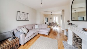 Ein Wohnzimmer mit Ecksofa, Kamin, Essbereich und einer Küche im Hintergrund.