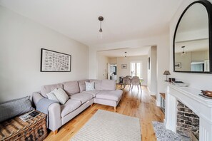 Ein Wohnzimmer mit Ecksofa, Kamin, Essbereich und einer Küche im Hintergrund.