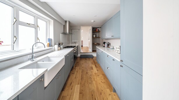 Eine moderne Küche mit großem Fenster, weißen Schränken und Holzboden.
