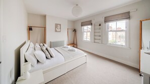 Ein Schlafzimmer mit Bett, Nachttisch, Lampe, Fenster mit Vorhängen, Heizkörper und einer Pendelleuchte.