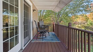 Una terraza techada con una mesa y sillas, vista a árboles y baranda de madera.
