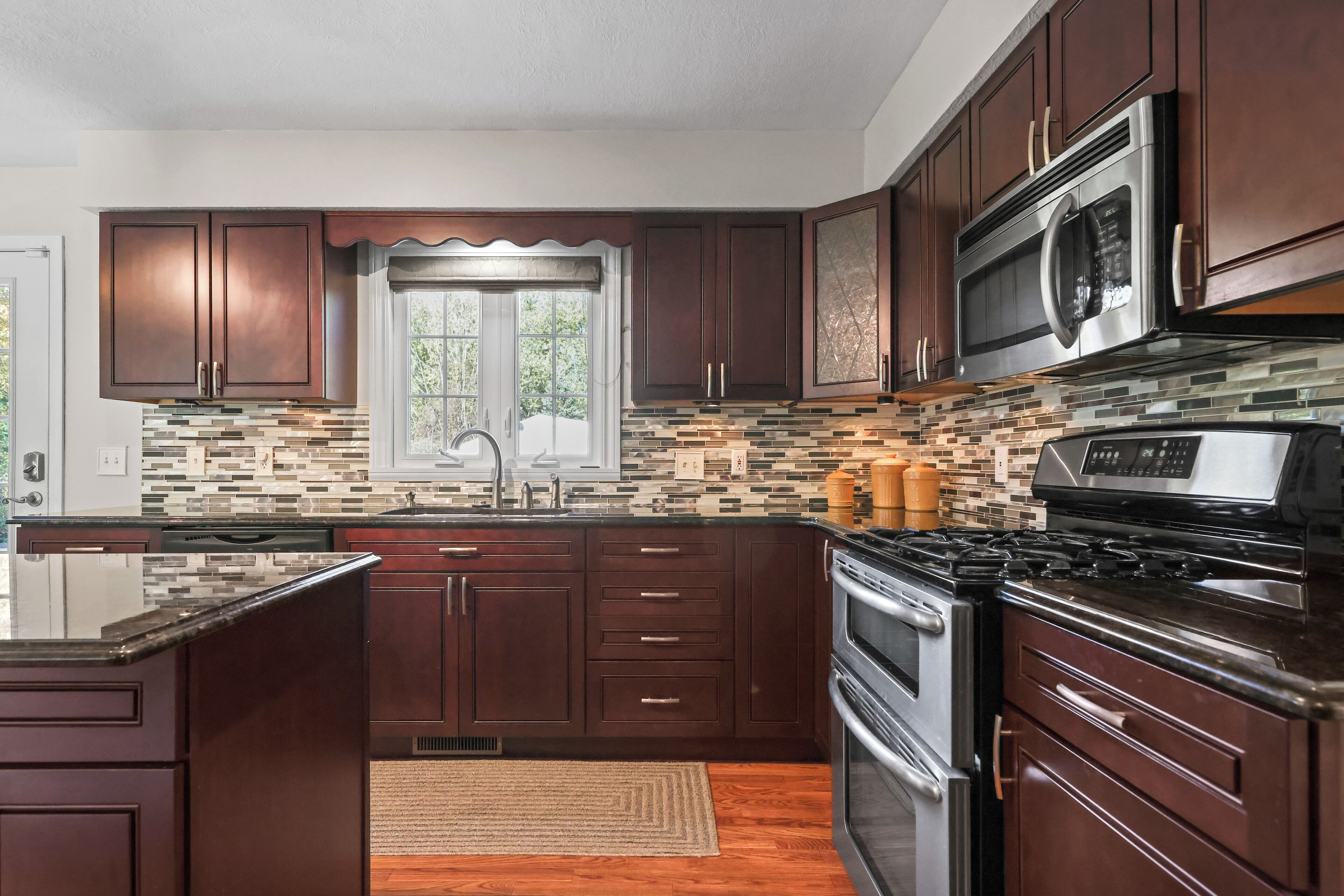 A kitchen with dark wooden cabinets, a stainless steel microwave, and a tiled backsplash.