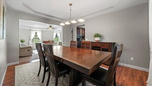 Un comedor con una gran mesa de madera, sillas, ventilador de techo y vistas al exterior.
