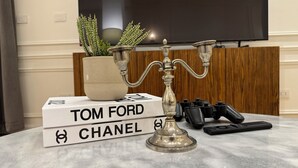 Marmorinen pöytä, jonka päällä on koristeellinen kynttelikkö, ruukkukasvi ja pino kirjoja, joiden otsikko on »TOM FORD CHANEL».