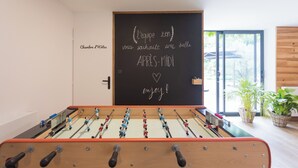 A foosball table in a room with a blackboard displaying a message in French, a door labeled 'Chambre d'Îlots,' and a view of a building outside. - Family home, a haven of peace at the foot of the Vercors mountains (Vif)