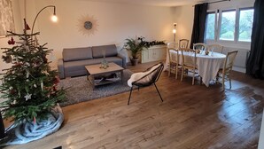 A living room with a sofa, a dining table with chairs, a Christmas tree, and a sunburst wall decoration. - Family home, a haven of peace at the foot of the Vercors mountains (Vif)