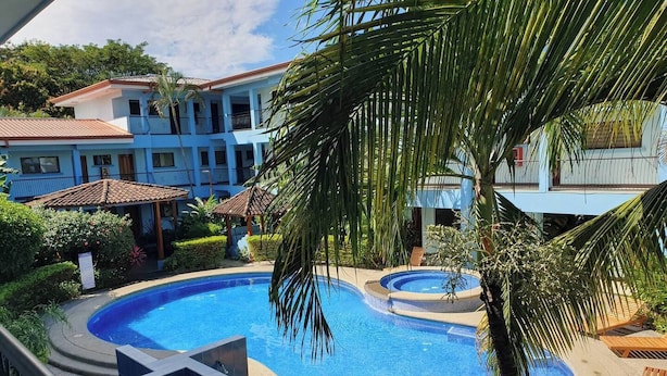 Una piscina con idromassaggio, circondata da palme e un edificio con balconi.