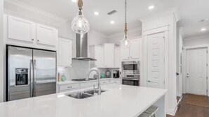 A modern kitchen with white cabinetry, stainless steel appliances, a central island with a sink, and pendant lighting. - New 3BR/2.5 LSV Heated Pool - Pearl at Prominence (Santa Rosa Beach)