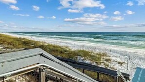 A beach view with a clear sky, sandy shore, and a building with a sloped roof. - New 3BR/2.5 LSV Heated Pool - Pearl at Prominence (Santa Rosa Beach)
