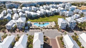 A coastal residential area with multiple white houses, a central swimming pool, and a beach in the background. - New 3BR/2.5 LSV Heated Pool - Pearl at Prominence (Santa Rosa Beach)