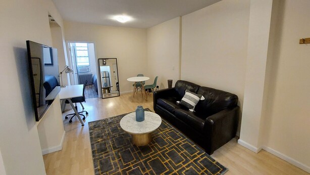 Un salon avec un canapé en cuir noir, une table basse ronde, une petite table blanche et un tapis à motifs.