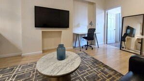 Un salon moderne doté d’un téléviseur à écran plat, d’un bureau avec une chaise, d’une table basse ronde et d’un grand miroir.
