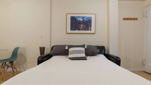 Une chambre à coucher avec un grand lit, une chaise, un porte-manteau et un tableau encadré au mur.