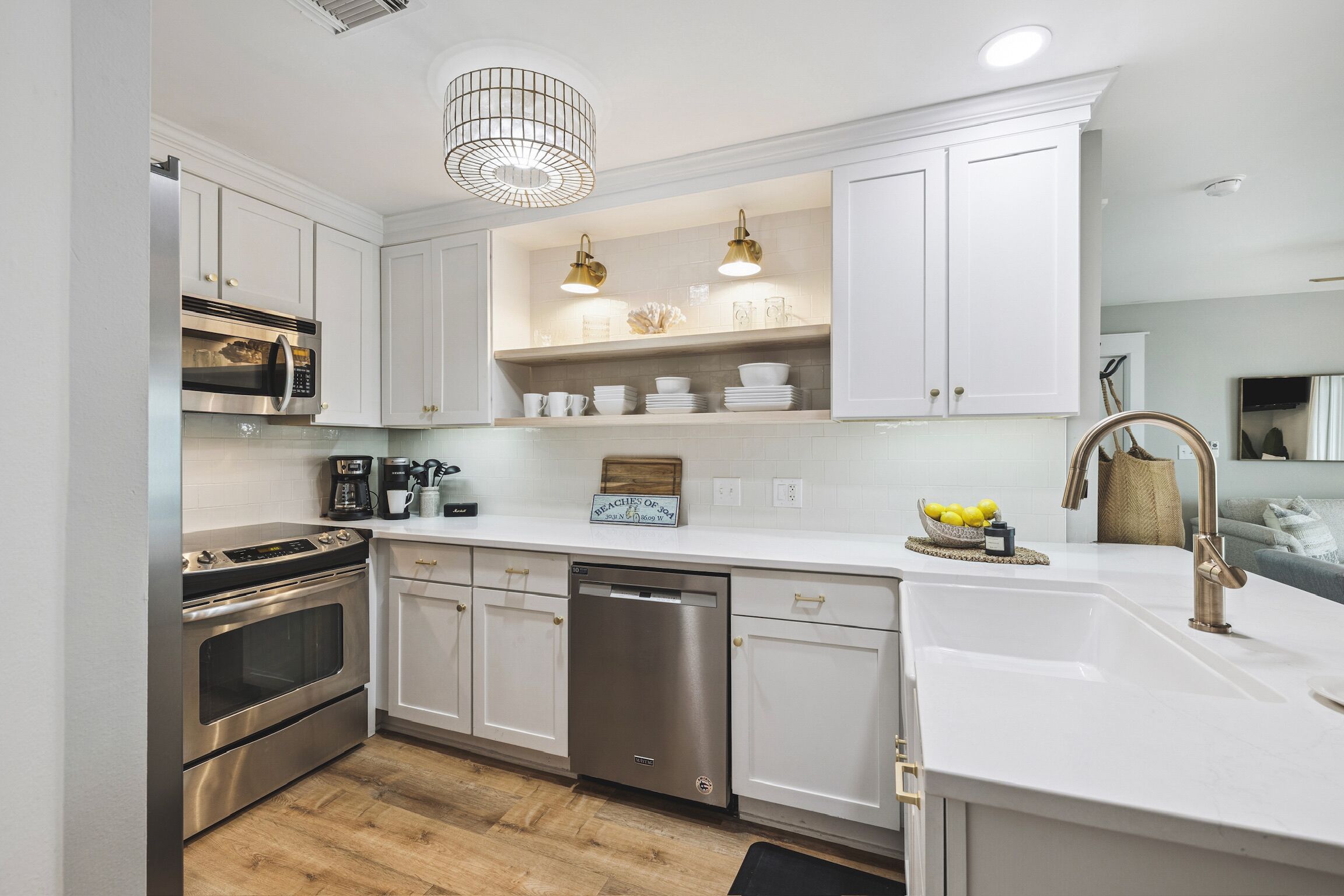 Une cuisine moderne avec des meubles blancs, des appareils en acier inoxydable et des luminaires suspendus.