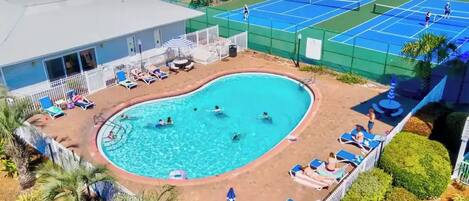 A swimming pool surrounded by lounge chairs and a tennis court.