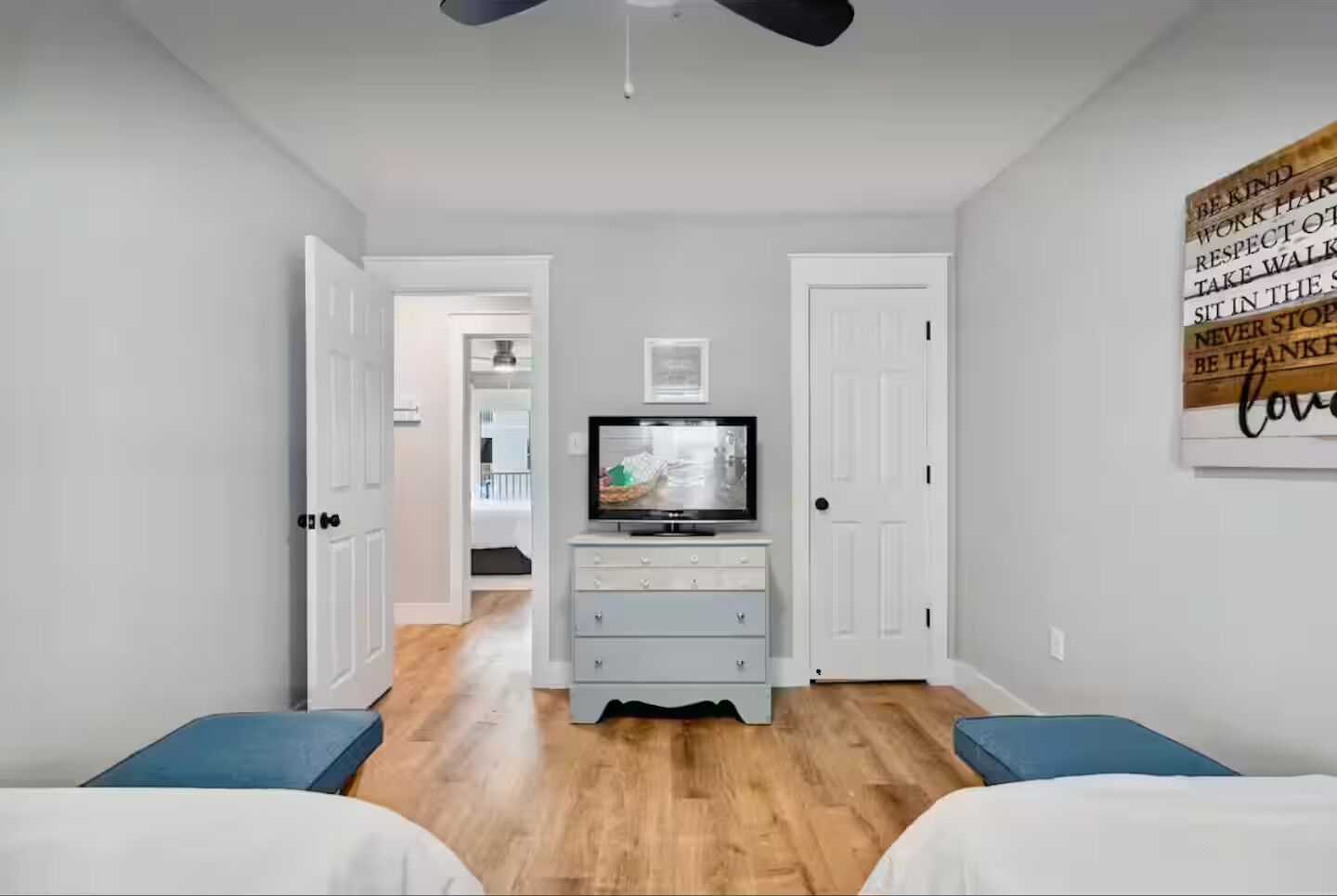 Quarto com televisão em uma cômoda, duas camas e corredor que dá para outro espaço.