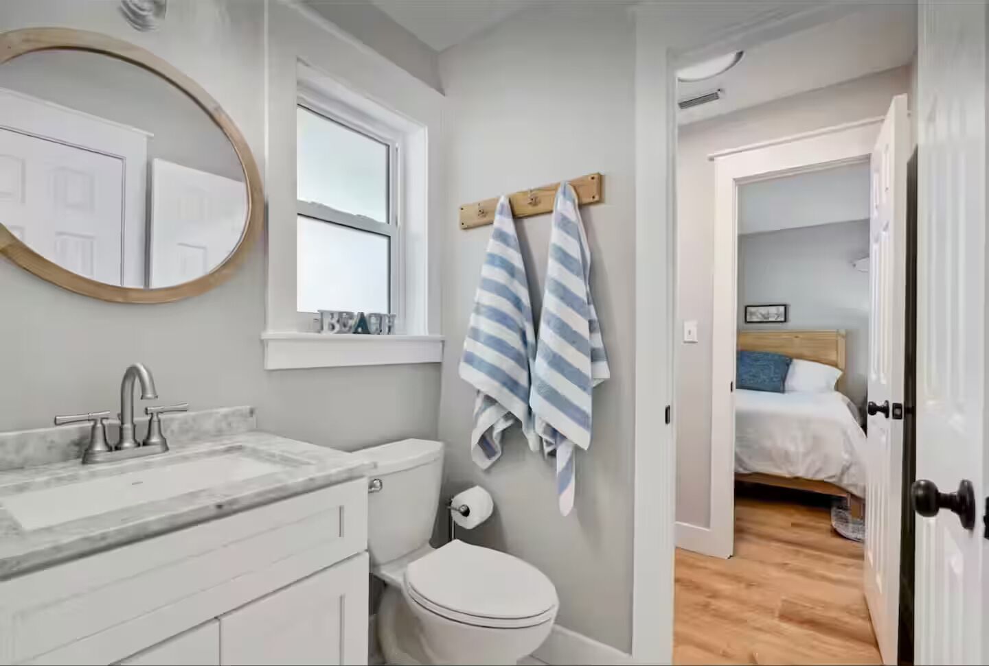 A bathroom with a sink, toilet, and a mirror. There is a window above the toilet and a towel rack with towels.