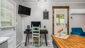 A compact room with a desk, chair, TV, and a wooden table with a lamp. - New-Sunfish Cottage - Walk to Hidden Harbor Marina (Smithville)