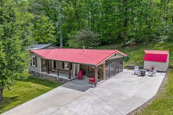 A two-story house with a red roof, a covered porch, and a small shed.