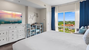 A bedroom with a large bed, a desk with a chair, a TV, and a window with a view.
