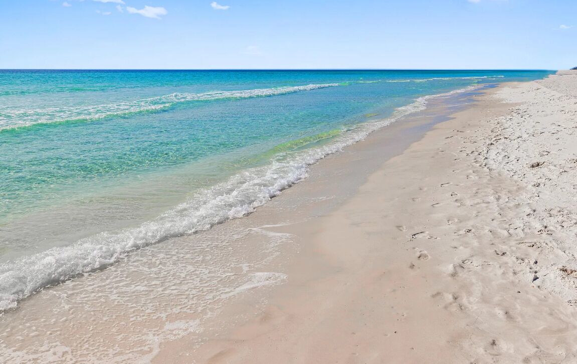 A beach with clear water, sandy shore, and a clear sky.