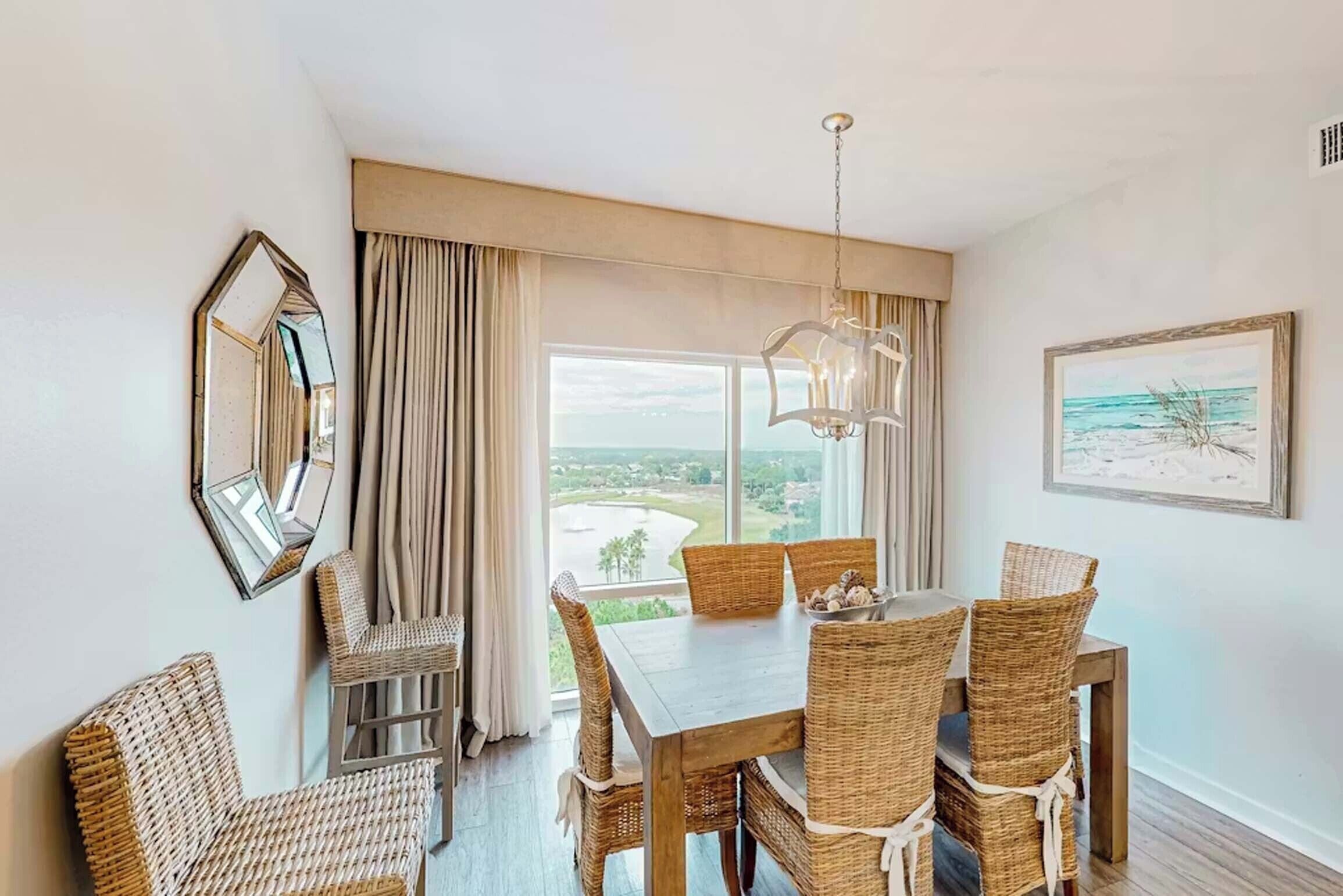 A dining area with a table and chairs, a chandelier, a large window with a view, and a framed picture on the wall.