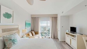 A hotel room with a bed, a TV, a desk, a window with curtains, and a view of the city. - ☀️🌴Cozy Studio w/ Gulf Views | Walk to Beach | Lagoon Pool | Luau II 6834 (Miramar Beach)