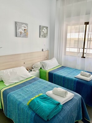 Ein Hotelzimmer mit zwei Betten, jeweils mit einer blauen gesteppten Tagesdecke und weißen Kissen. An den Wänden hängen zwei Bilder mit floralen Motiven.