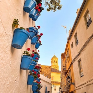 A narrow street with buildings on either side, a bell tower in the background, and blue flower pots on the wall. - Diana 507 - BeachFront Studio with Sun All Day (Marbella)