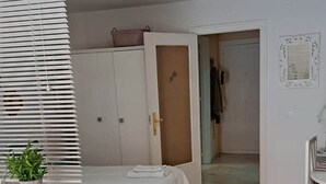 Een slaapkamer met een bed, een bureau, een kamerplant, een kledingkast en een deur naar een andere kamer.