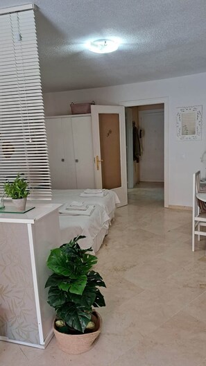 Ein Schlafzimmer mit einem Bett, einem Schreibtisch, einer Zimmerpflanze, einem Kleiderschrank und einer Tür zu einem anderen Raum.