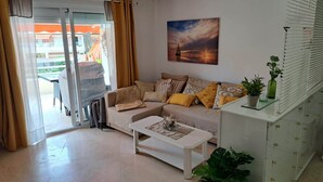 Een woonkamer met een bank, een salontafel, een schilderij, een plant en een schuifdeur naar een buitenruimte.
