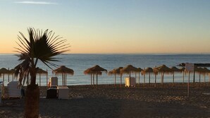 Een strand met rieten parasols, een palmboom en strandstoelen.