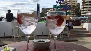 Twee glazen verfrissende drankjes op een tafel, samen met een smartphone en een aansteker.