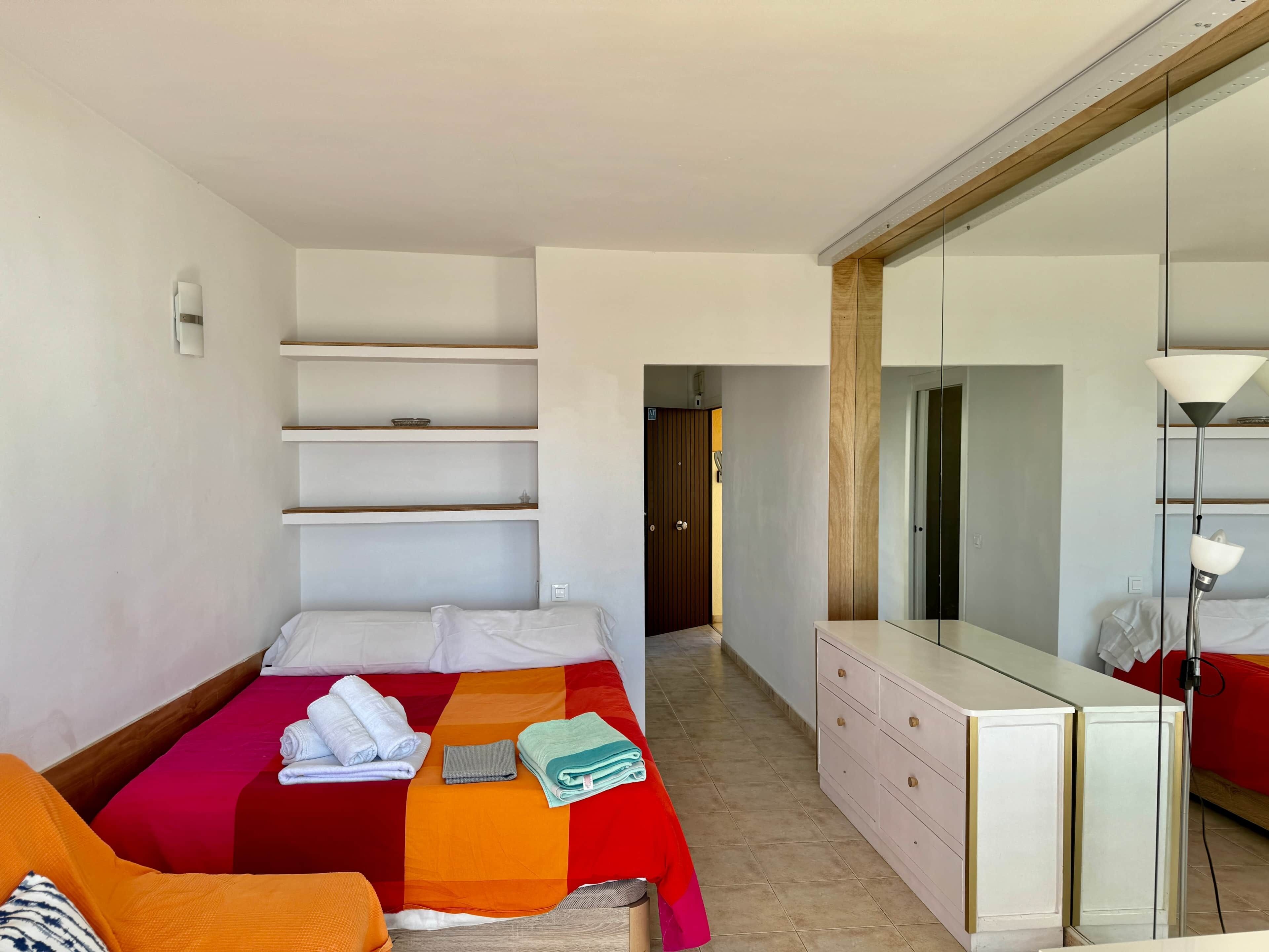 A hotel room with a bed, a dresser, a mirror, and a hallway leading to another room.