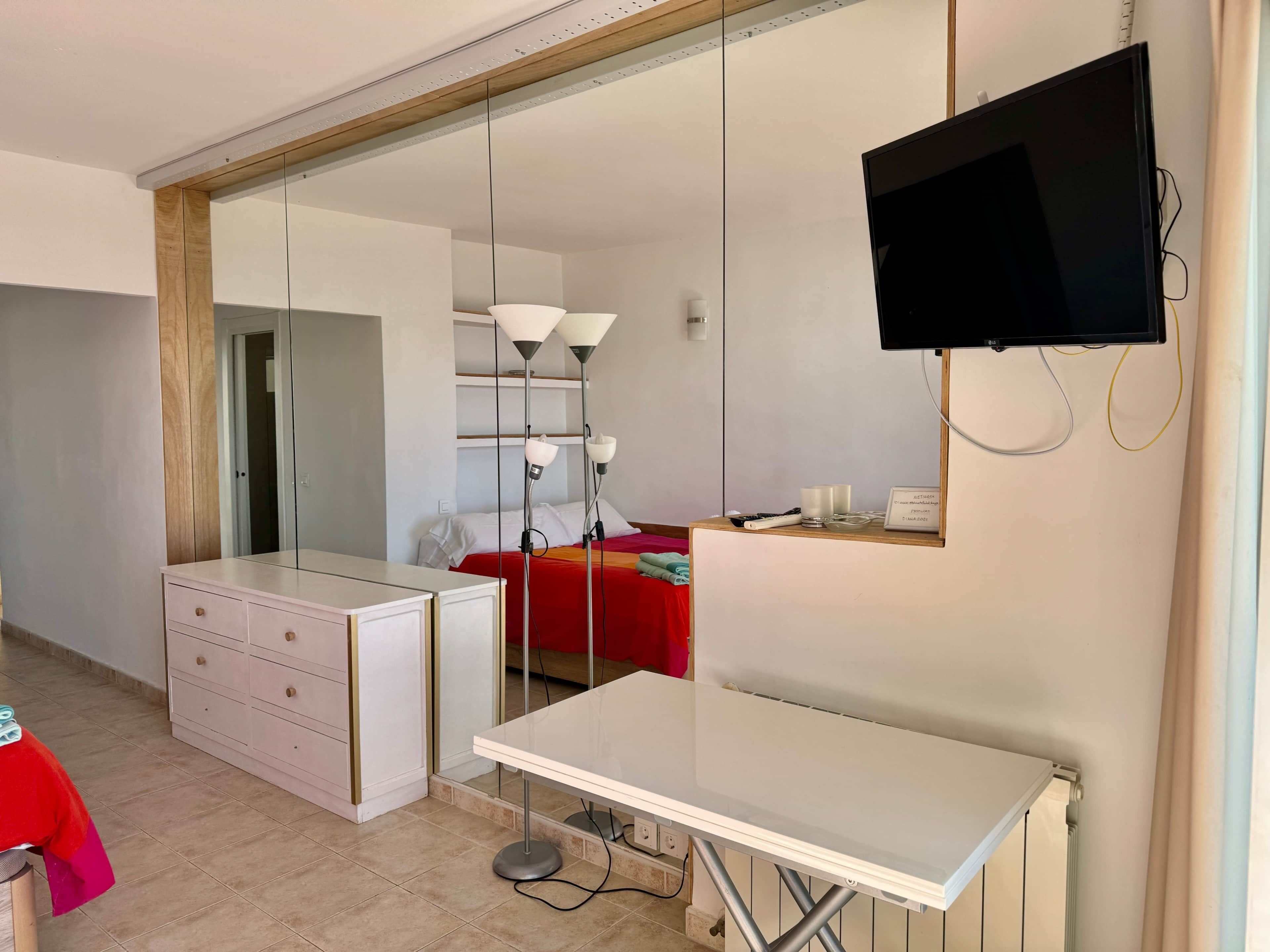 Une chambre d’hôtel équipée d’un lit, d’un bureau, d’une commode, d’une télévision et d’un grand miroir.