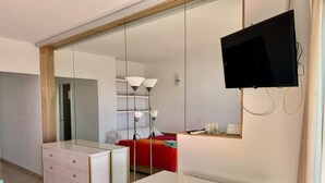 Een hotelkamer met een bed, een bureau, een dressoir, een televisie en een grote spiegel.